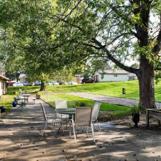 A sunny outdoor patio with tables and chairs surrounded by trees and a green landscape.