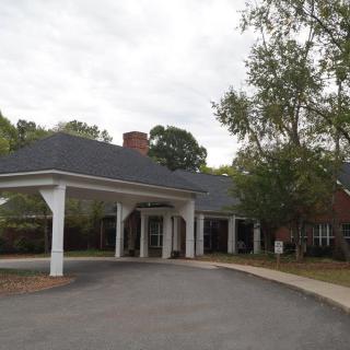 A building with a covered entrance and a driveway, surrounded by trees.