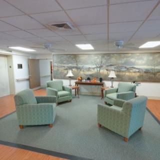 A cozy lobby with green upholstered chairs arranged around a carpet, featuring a scenic mural on the wall.