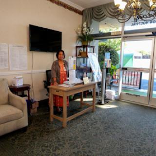 A welcoming lobby with a woman standing behind a table, adorned with plants and soft furniture.