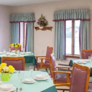 A neatly arranged dining area with tables set, featuring colorful flowers and large windows with curtains.
