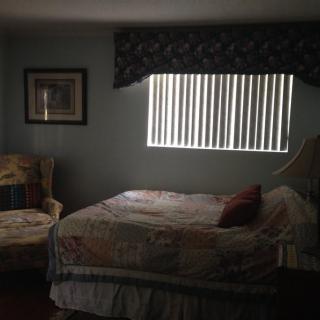 A cozy bedroom with a bed, armchair, and window blinds.