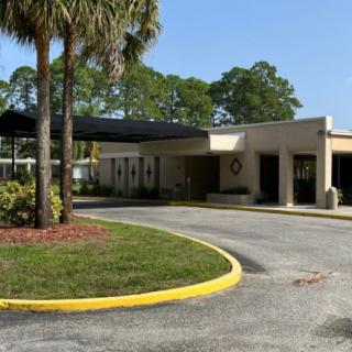 A building with a driveway and surrounding palm trees on a sunny day.