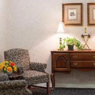 A cozy living room corner with an armchair, a side table adorned with a lamp and decorative plants.