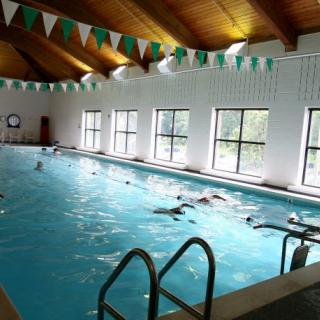 People swimming in an indoor pool with wooden ceiling and natural light.