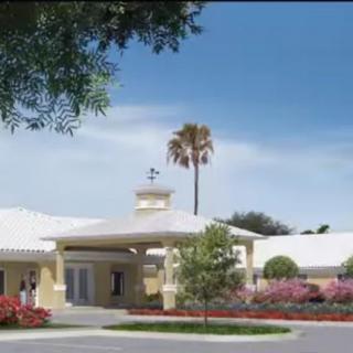 A building with a prominent entrance surrounded by landscaping and a tall palm tree under a cloudy sky.