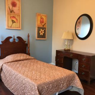 A cozy bedroom with a single bed, wooden furniture, and decorative floral art on the walls.