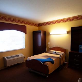A simple hotel room featuring a bed, a window with curtains, and basic furniture.