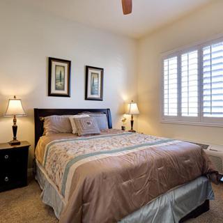 A cozy bedroom with a neatly made bed, flanked by two lamps and decorative wall art.