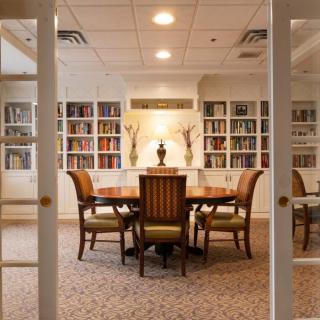 An elegant library with a wooden table and chairs, surrounded by bookshelves.