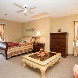 A spacious bedroom with a large bed, a dresser, and a coffee table under warm lighting.