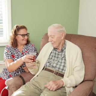 A caregiver assists an elderly man in a comfortable home setting.