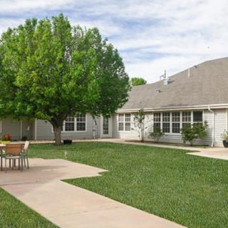 A serene backyard with a well-maintained lawn, trees, and outdoor seating area.