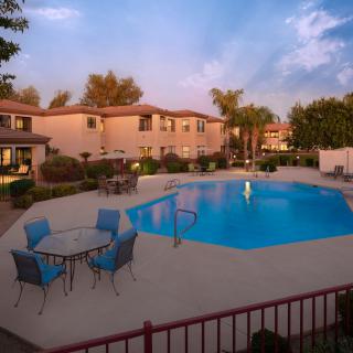 A serene outdoor view of a residential swimming pool surrounded by trees and patio furniture, located in an apartment complex.