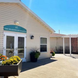 The entrance to a building with a pathway and flower pots on a sunny day.