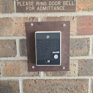 A doorbell mounted on a brick wall with a sign requesting visitors to ring it for entry.