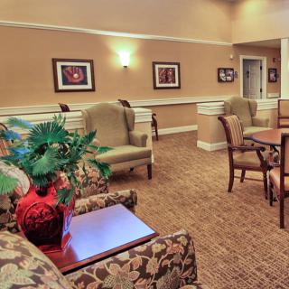 A cozy seating area with comfortable chairs and a table, decorated with paintings and plants.