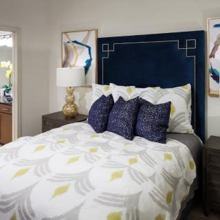 A stylish bedroom with a modern design featuring a blue headboard, decorative pillows, and contemporary artwork.