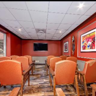 A small conference room with rows of chairs facing a television, adorned with colorful artwork on the walls.