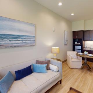 A modern and cozy living room with a sofa, artwork on the wall, and an adjoining kitchen area.