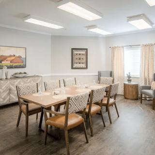 A modern dining room with a large wooden table, comfortable chairs, and wall art under soft lighting.
