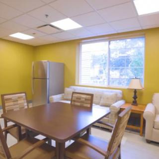 A cozy kitchen and dining area with a table, chairs, sofa, refrigerator, and large window.