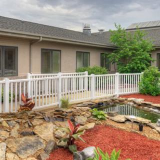 A beautifully landscaped backyard featuring a small pond and rock garden, bordered by a white picket fence.