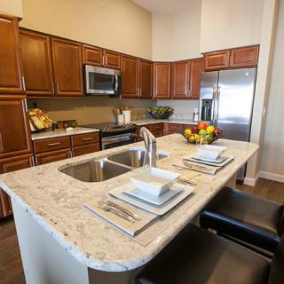 A modern kitchen with a central island, equipped with stainless steel appliances and bar stools for dining.