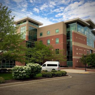 A modern office building surrounded by lush greenery under a partly cloudy sky.