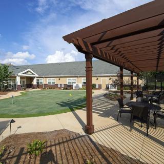 A sunny outdoor area with a pergola, seating, and a well-maintained lawn in front of a building.