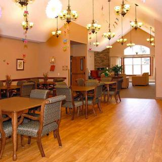 A spacious dining area with multiple tables and chairs, illuminated by elegant chandeliers and featuring a wooden floor.