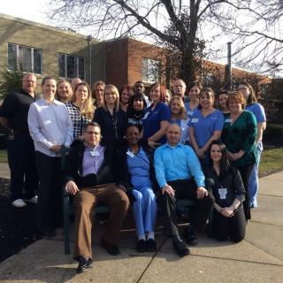 A group of people posing for a team photo outside on a sunny day.