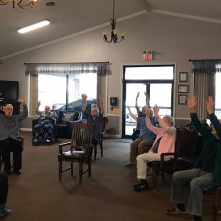A group of elderly people participating in a seated exercise session indoors.
