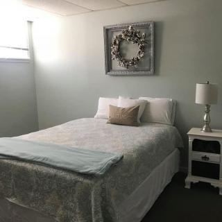 A minimalist bedroom with a neatly made bed, a nightstand with a lamp, and wall decor.