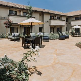 A sunny patio area with outdoor furniture and umbrellas in front of a residential building.