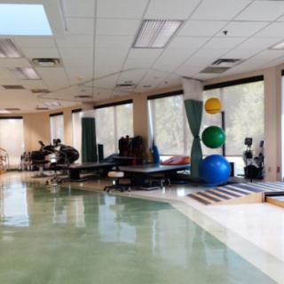 A spacious rehabilitation therapy room featuring exercise equipment and large windows for natural light.