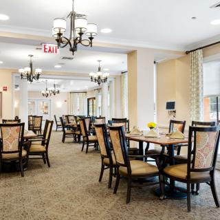 An elegant dining room with neatly arranged tables and chairs, featuring chandeliers and a carpeted floor.