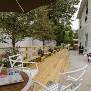 A peaceful outdoor patio with white chairs and tables, set against a wooden deck and surrounded by trees.