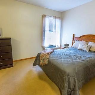A cozy bedroom with a neatly made bed, wooden dresser, and natural light coming through the window.