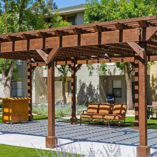A wooden pergola providing shade over an outdoor seating area in a garden setting.