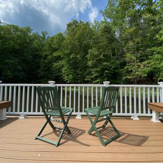 A tranquil deck featuring two green chairs facing a lush forest backdrop under a clear blue sky.