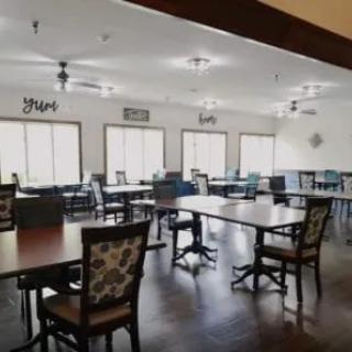 A spacious dining room with several arranged tables and chairs, well-lit by natural light from multiple windows.