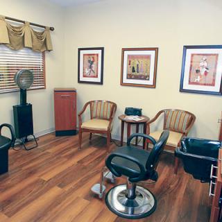 A cozy hair salon interior with wooden floors, stylish chairs, and framed artwork on the walls.