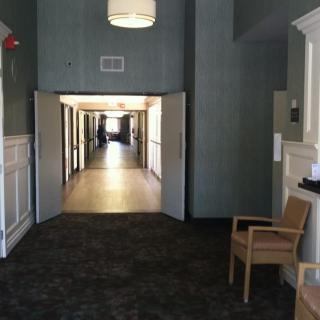 A well-lit hallway with open doors and a single chair placed to the side.