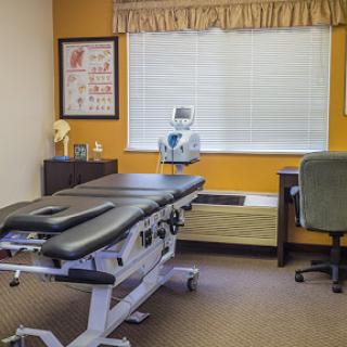 An organized medical office featuring a treatment table and a work desk.