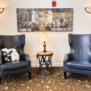 A cozy living room setup with two blue chairs and a side table with a lamp, adorned by a cityscape artwork on the wall.