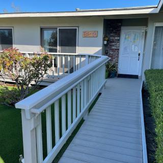 A house entrance with a wooden ramp and white railing leading to the front door.
