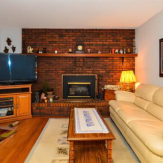 A cozy living room with a brick wall and fireplace, featuring a comfortable sofa, television, wooden coffee table, and warm lighting.