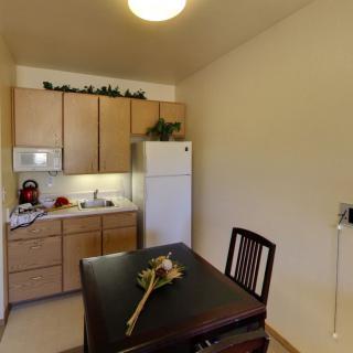 A small kitchen with a dining area, featuring a refrigerator, cabinets, and a microwave.