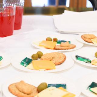 Plates of snacks with cheese, crackers, and olives, accompanied by red drinks.